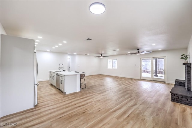 kitchen with light wood-type flooring, a kitchen island with sink, a kitchen breakfast bar, stainless steel dishwasher, and open floor plan