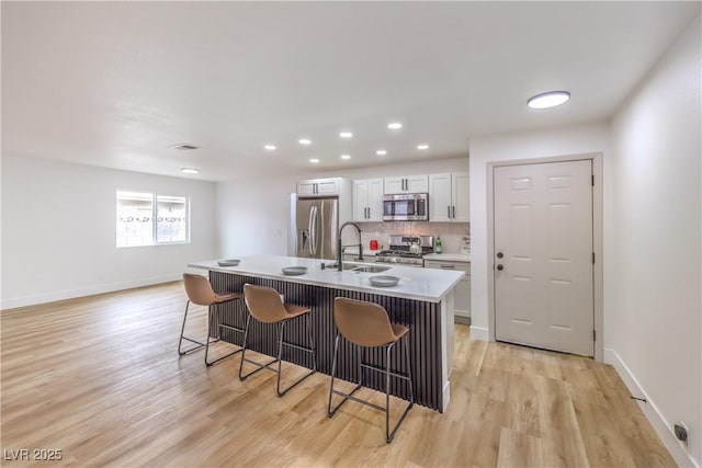 kitchen with backsplash, a breakfast bar area, light wood-style flooring, stainless steel appliances, and a sink