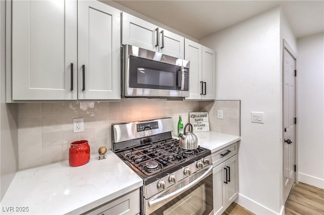 kitchen with light stone countertops, baseboards, stainless steel appliances, decorative backsplash, and light wood-type flooring