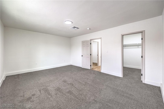 unfurnished bedroom featuring visible vents, a walk in closet, dark carpet, a closet, and baseboards