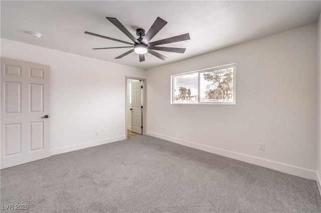 carpeted spare room featuring baseboards and a ceiling fan