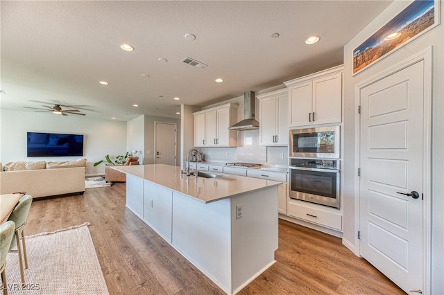 kitchen featuring visible vents, wall chimney range hood, light wood-type flooring, stainless steel appliances, and a sink