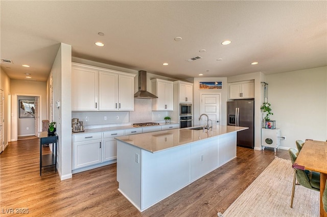 kitchen with visible vents, a sink, white cabinets, appliances with stainless steel finishes, and wall chimney range hood