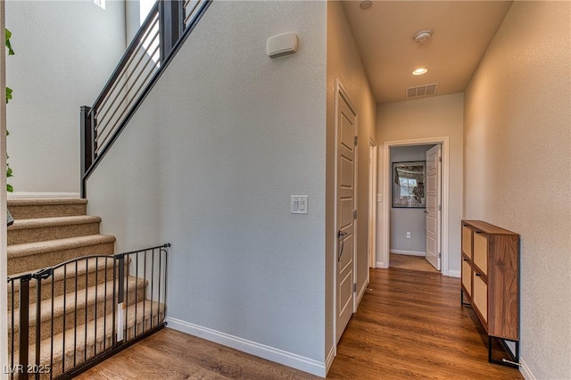 hallway with stairs, visible vents, wood finished floors, and baseboards