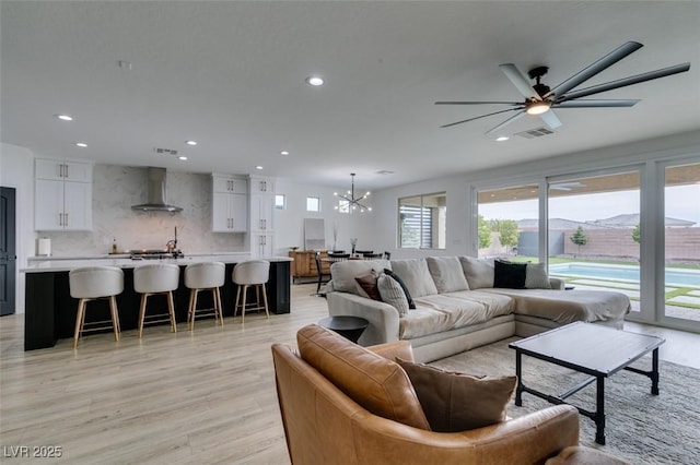 living area featuring recessed lighting, light wood-type flooring, visible vents, and ceiling fan with notable chandelier