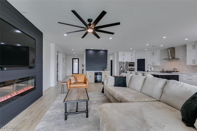 living room with beverage cooler, recessed lighting, light wood-style flooring, a fireplace, and a ceiling fan