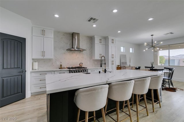 kitchen with visible vents, tasteful backsplash, white cabinetry, wall chimney exhaust hood, and range