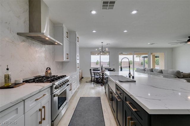 kitchen featuring visible vents, white cabinets, wall chimney exhaust hood, and stainless steel stove