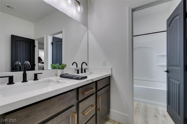 full bath featuring double vanity, visible vents, wood finished floors, and a sink