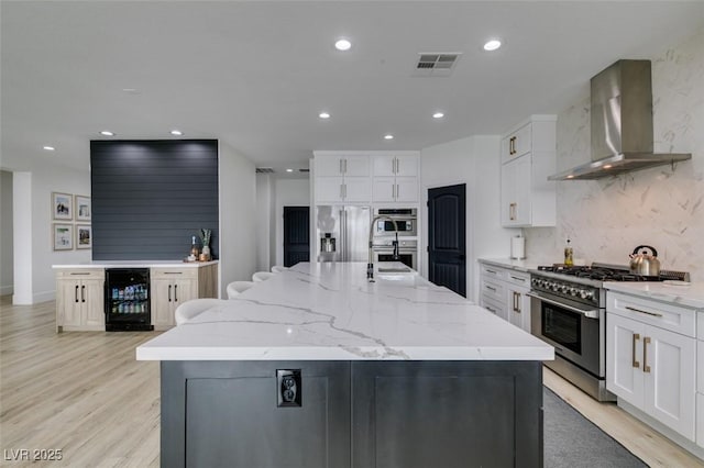 kitchen with visible vents, wine cooler, a large island, stainless steel appliances, and wall chimney exhaust hood