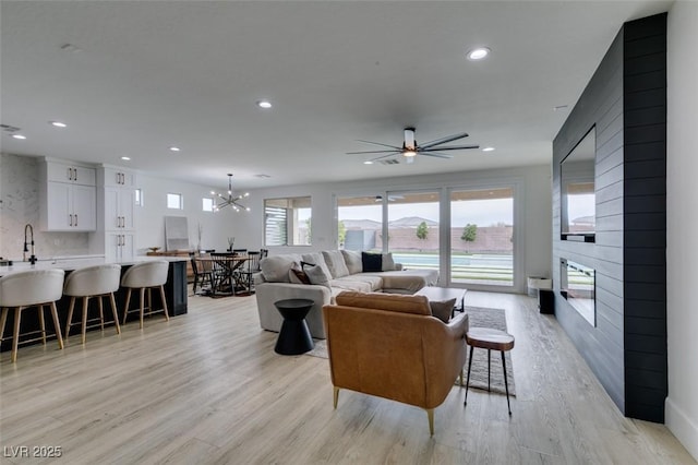 living room with recessed lighting, ceiling fan with notable chandelier, a fireplace, and light wood-style floors