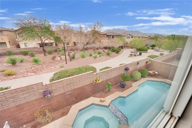 view of swimming pool with a residential view, a fenced backyard, and a pool with connected hot tub