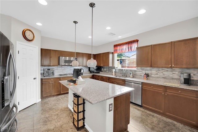 kitchen with visible vents, a sink, light stone counters, a kitchen island, and stainless steel appliances