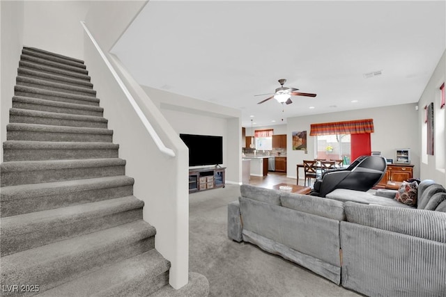 living area featuring stairway, a ceiling fan, visible vents, recessed lighting, and light colored carpet