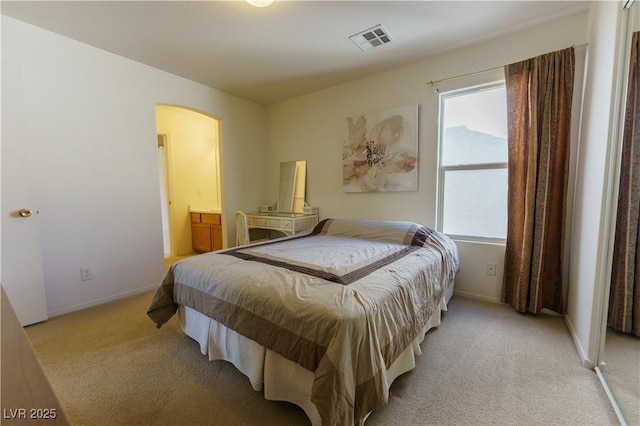 bedroom featuring arched walkways, visible vents, light colored carpet, and baseboards