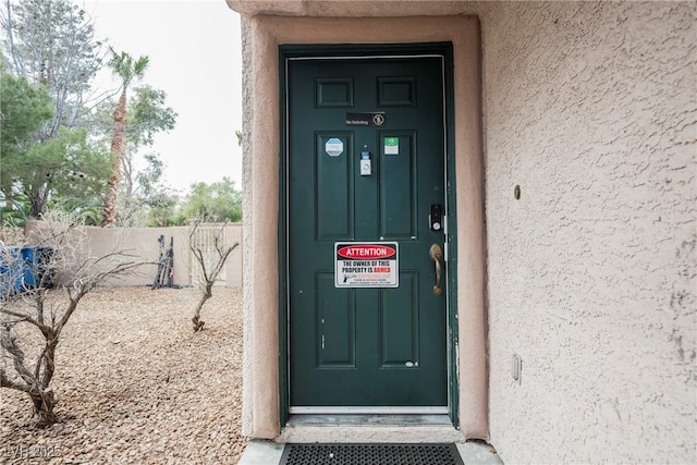 entrance to property featuring stucco siding and fence