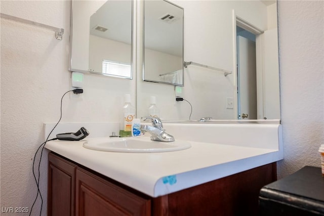 bathroom with visible vents, vanity, and a textured wall