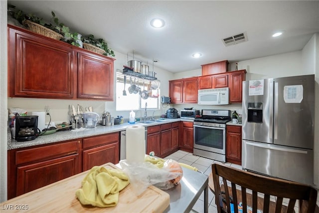 kitchen featuring a sink, reddish brown cabinets, appliances with stainless steel finishes, light countertops, and light tile patterned floors