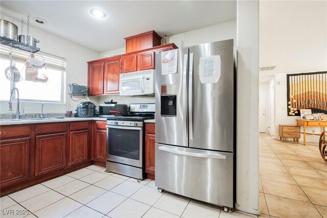 kitchen with light tile patterned floors, visible vents, a sink, stainless steel appliances, and reddish brown cabinets