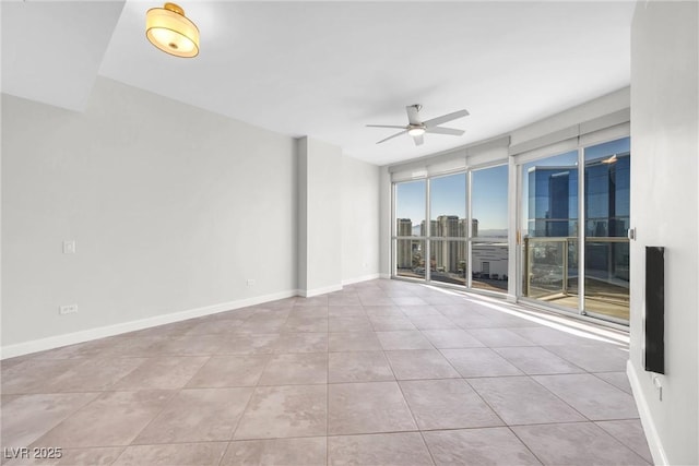 unfurnished room with baseboards, a wall of windows, tile patterned floors, a view of city, and a ceiling fan