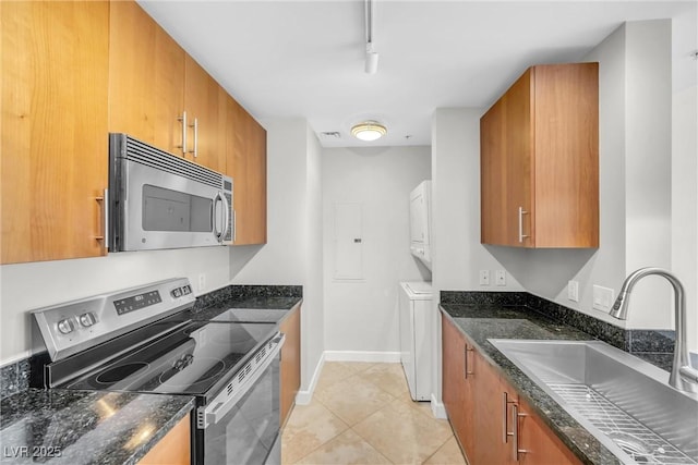 kitchen featuring brown cabinetry, stacked washer / drying machine, appliances with stainless steel finishes, and a sink