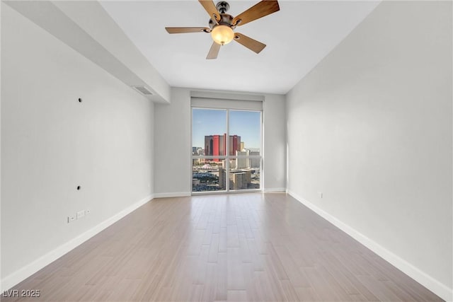 empty room featuring baseboards, a city view, wood finished floors, and a ceiling fan