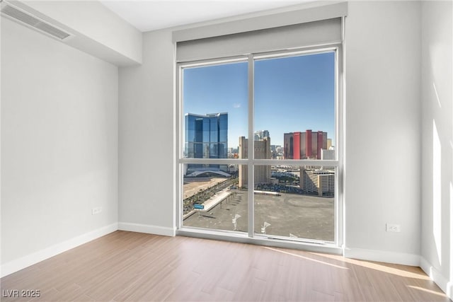 spare room with visible vents, a city view, baseboards, and wood finished floors