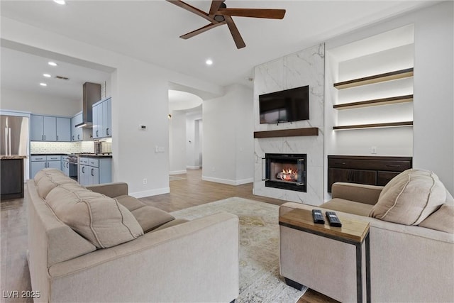 living room with light wood finished floors, recessed lighting, arched walkways, and a high end fireplace