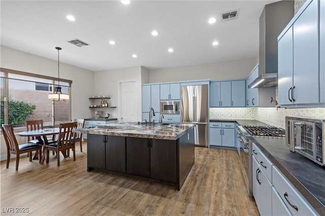 kitchen featuring wall chimney range hood, visible vents, appliances with stainless steel finishes, and light wood-type flooring