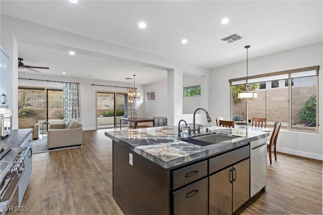 kitchen featuring visible vents, a sink, a center island with sink, stainless steel appliances, and dark wood-style flooring