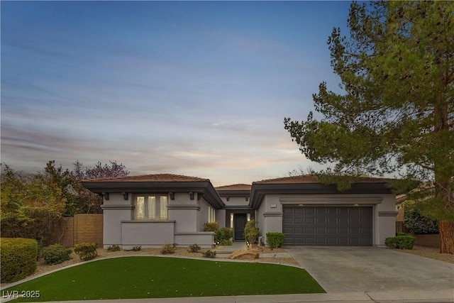 prairie-style house with an attached garage, fence, driveway, and stucco siding