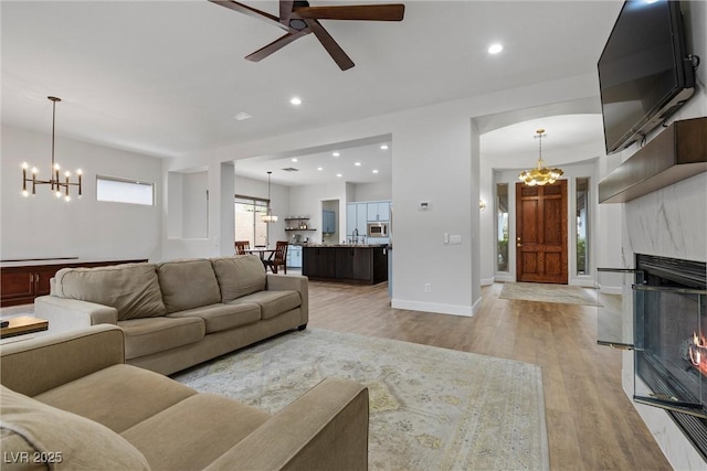 living room featuring baseboards, a premium fireplace, light wood-style flooring, recessed lighting, and arched walkways