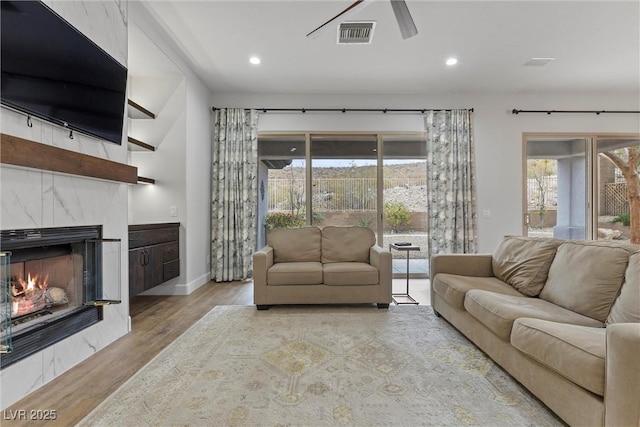 living room featuring a high end fireplace, visible vents, a wealth of natural light, and wood finished floors