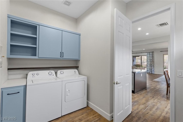 washroom featuring washing machine and clothes dryer, visible vents, cabinet space, and wood finished floors