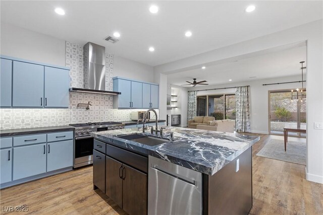 kitchen featuring a sink, appliances with stainless steel finishes, wall chimney range hood, tasteful backsplash, and light wood-type flooring