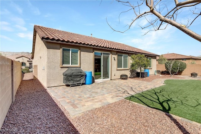 rear view of property featuring a tiled roof, stucco siding, a lawn, a fenced backyard, and a patio area