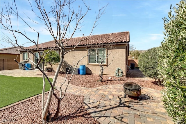 rear view of house featuring a fire pit, fence, a tile roof, stucco siding, and a patio