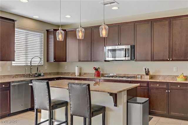 kitchen with visible vents, a sink, a kitchen island, stainless steel appliances, and a breakfast bar area