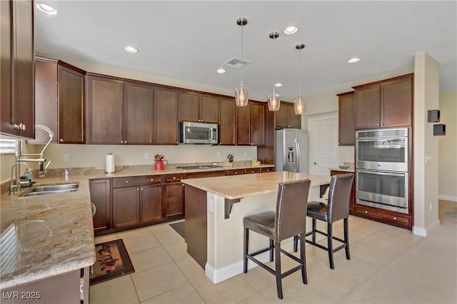 kitchen with visible vents, a center island, a breakfast bar, stainless steel appliances, and a sink