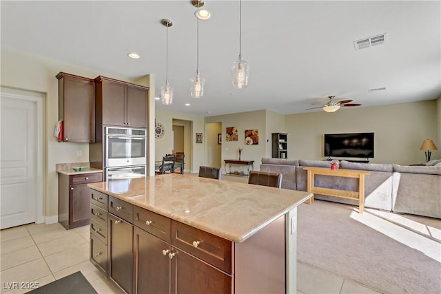 kitchen with visible vents, a kitchen island, light tile patterned flooring, double oven, and decorative light fixtures