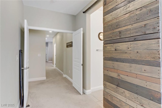 corridor featuring a barn door, light carpet, and baseboards