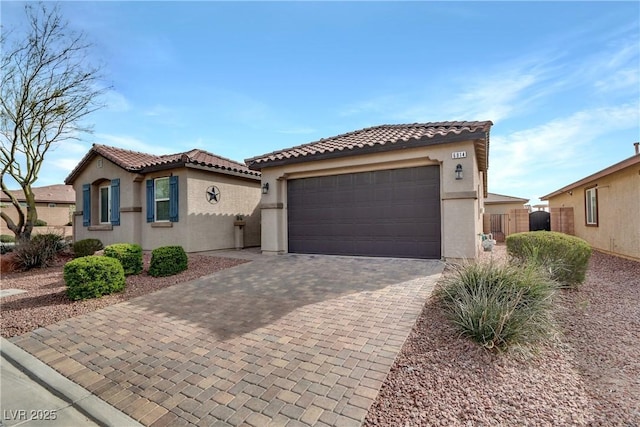 mediterranean / spanish-style house with fence, a tiled roof, stucco siding, decorative driveway, and a garage