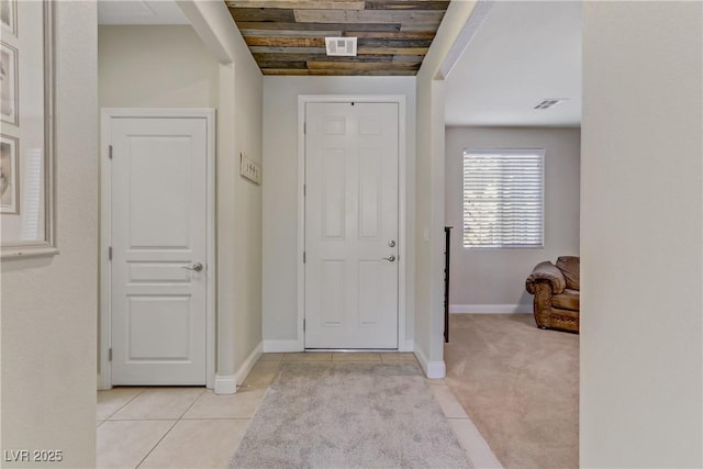 foyer entrance featuring visible vents, wooden ceiling, light tile patterned floors, baseboards, and light colored carpet