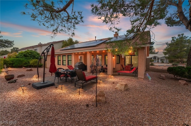 back of house with a patio area, roof mounted solar panels, stucco siding, and fence