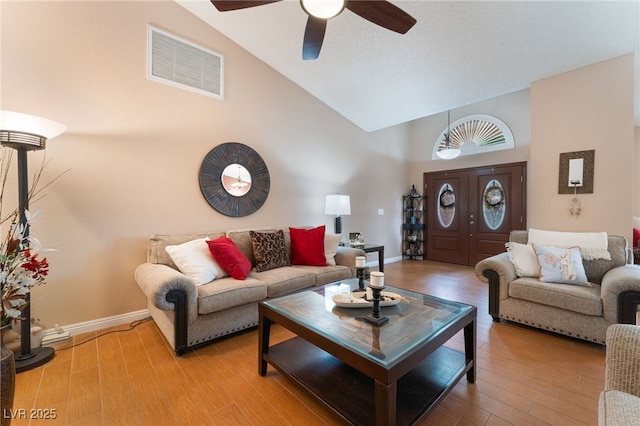 living area featuring wood finished floors, baseboards, a ceiling fan, visible vents, and high vaulted ceiling