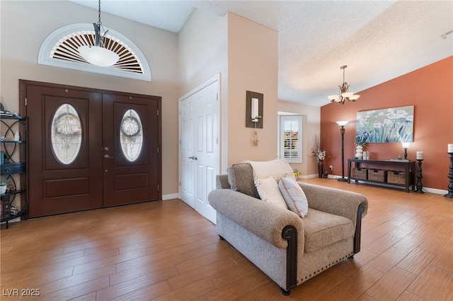 entryway featuring baseboards, a chandelier, lofted ceiling, wood finished floors, and a textured ceiling