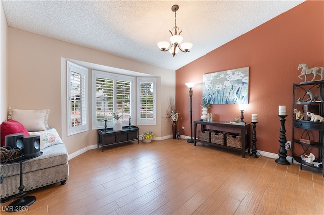 sitting room featuring light wood finished floors, a textured ceiling, an inviting chandelier, and vaulted ceiling