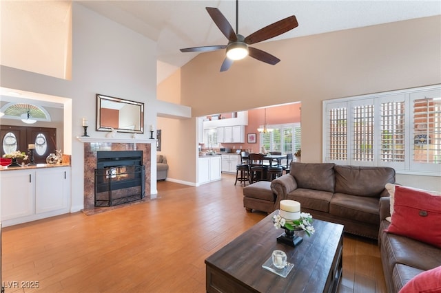 living area with a high end fireplace, light wood finished floors, high vaulted ceiling, and a ceiling fan