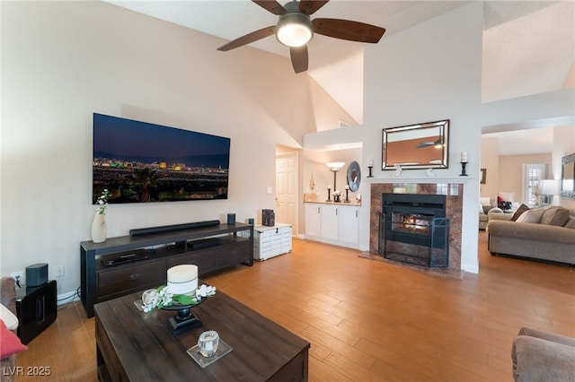 living area with wood finished floors, a ceiling fan, a high end fireplace, and high vaulted ceiling