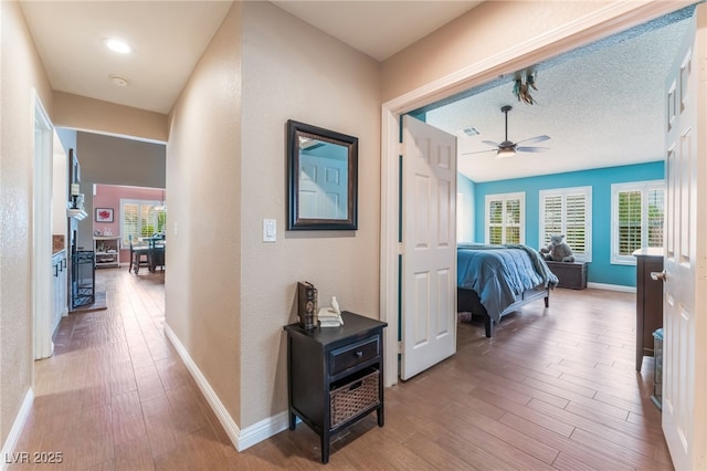 corridor featuring visible vents, baseboards, a textured ceiling, and wood finished floors